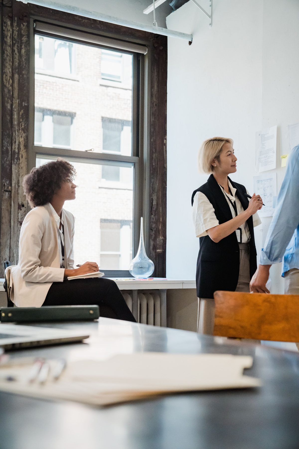 Two consultants at a window reviewing a wall of process notes during a client session